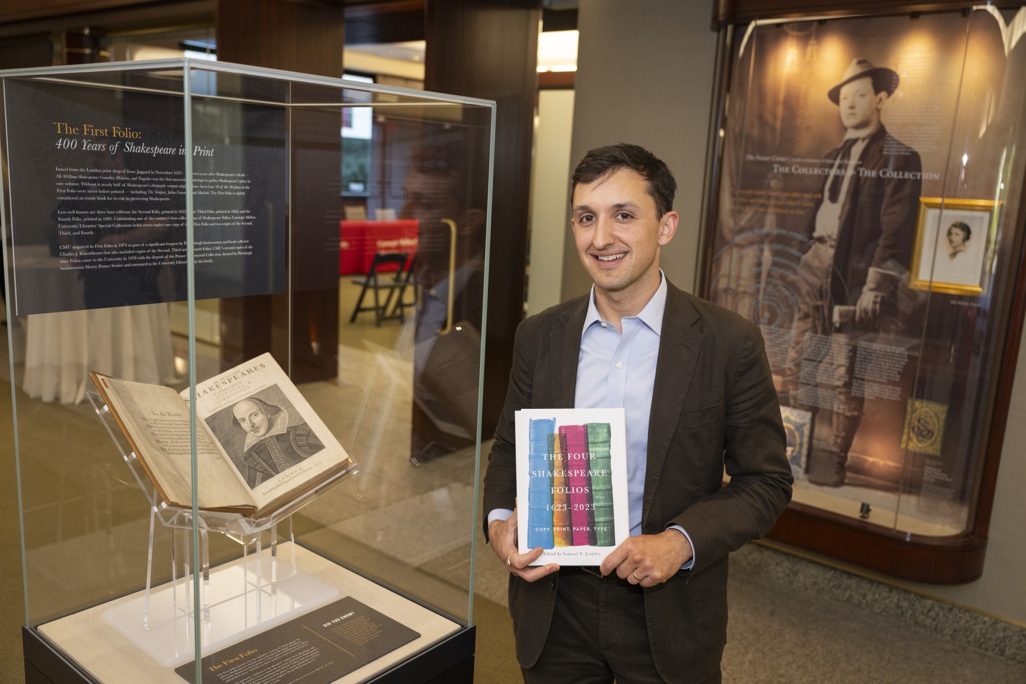 A person wearing a suit is standing in front of a glass case with a shakespeare folio in it.