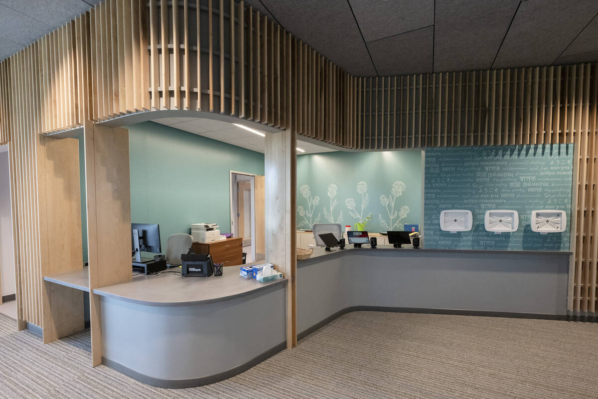 A curved reception desk done in blue and gray has computers, ipads and other materials sitting on it. The wall is done in blond wood slats around the desk.