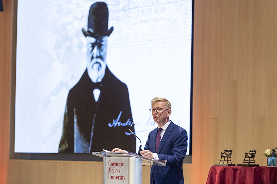 Dean Webster stands at a podium in front of a large photo of Andrew Carnegie.